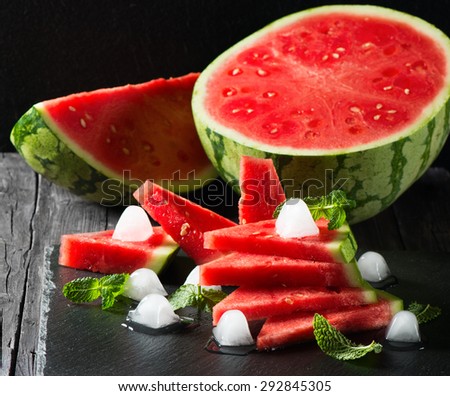 Seedless ripe watermelon cut slices with mint and ice on a black background