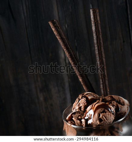 Close up of scoops of chocolate ice cream with chocolate sauce and chips decorated with wafer biscuits on black background with copy space.