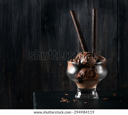 Chocolate ice cream with wafer sticks  with decorative chocolate chips and sauce  on a black background with space for text.