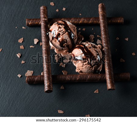 Chocolate ice cream with wafer sticks, chocolate chips and sauce on black background