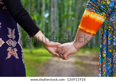 Couple of girlfriends holding by the hands, walking in the forest