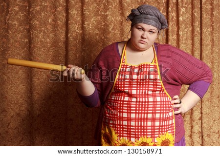 Young housewife holding rolling-pin in hand, looks angry
