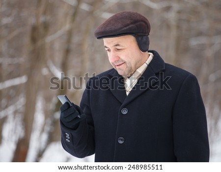 Middle aged man looking at mobile phone in the winter forest