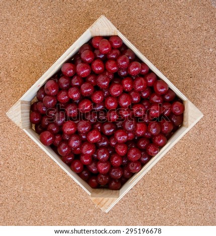 red cherries ready to deliver, loaded into a square wooden box,   oriented  as rhombus, against flat cork background