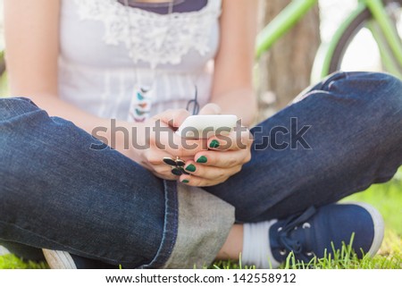 Close up of young woman sitting on the grass and using smart phone.