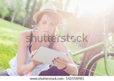 Beautiful young woman using digital tablet sitting next to her bike Beautiful young woman using digital tablet sitting next to her bike
