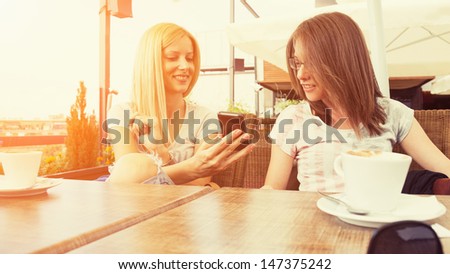 Girls enjoying sitting in cafe using smartphone Girls enjoying sitting in cafe using smartphone