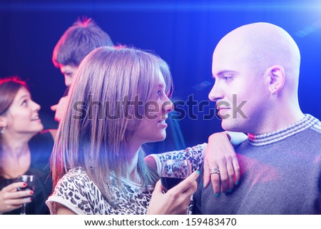Cheerful friends having conversation and enjoying in the nightclub. Beautiful couple looking each is in focus.