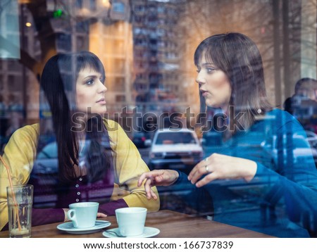 Two young girls having conversation in a cafe. The photo was taken through the window