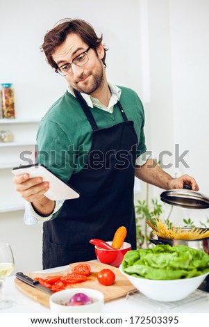 Handsome man preparing healthy food in the kitchen and reading the recipe using digital tablet.