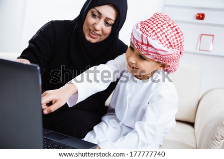 Happy Arabic mother and son together sitting on the couch and using laptop.