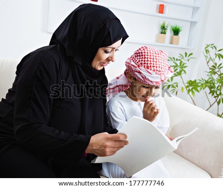Happy Arabic mother and son together sitting on the couch and reading a book.