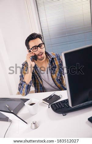 Young graphic designer working in office and having phone conversation.