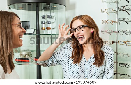 Happy Woman With Friend Examining Eyeglasses In Optician Store