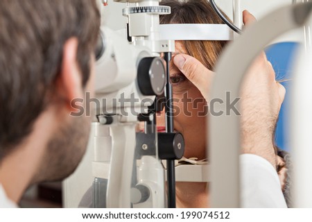 Ophthalmologist In Exam Room With Mature Woman Sitting In Chair Looking Into Eye Test Machine