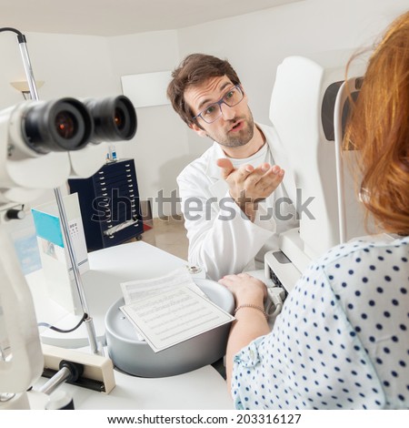 Ophthalmologist In Exam Room With Young Woman Sitting In Chair Looking Into Eye Test Machine