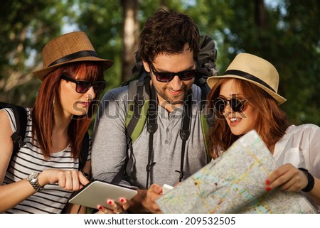 Three Young Tourists In Nature Browsing Map Using Digital Tablet