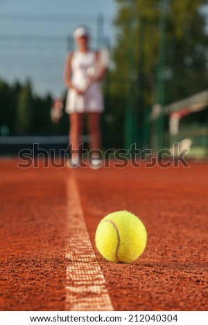 Female Tennis Player And Ball On Tennis Court. Focus Is On Tennis Ball