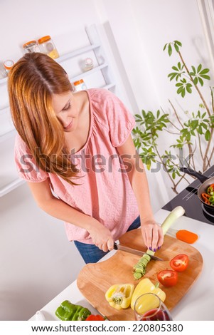 Beautiful Young Housewife In The Kitchen Slicing Vegetables On Chopping Board