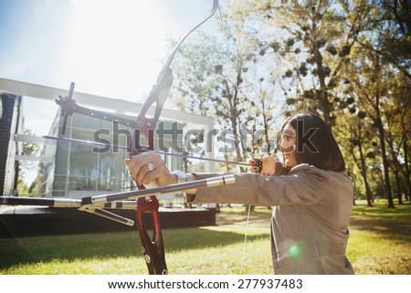 Businesswoman Pointing The Target With Bow And Arrow In Front Of Business Building