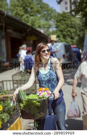 Female Is Going From Market Place With Basket Full Of Vegetables And Bouquet Of Flowers