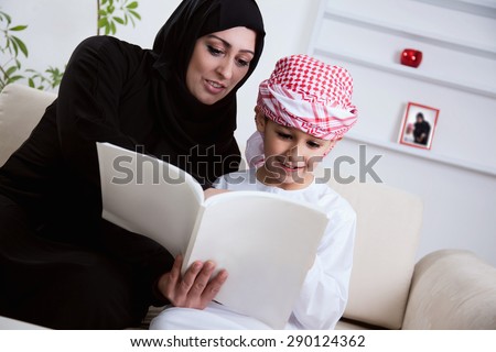 Arabic Mother And Son Together Sitting On The Couch And Reading A Book.