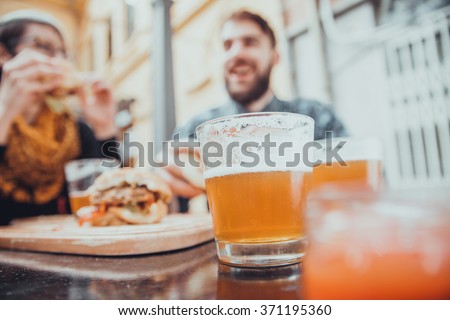 Couple In Fast Food Restaurant Eating Burgers. Focus Is On Glass Of Beer