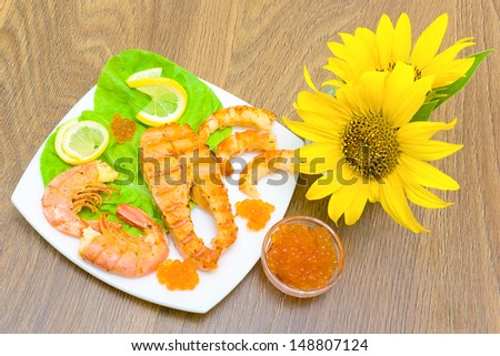 delicious piece of grilled fish with lemon, shrimp, red salmon caviar and a bouquet of sunflowers. horizontal photo.