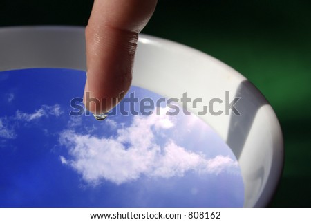 finger with water droplet in focus and sky inside it