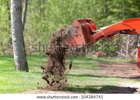 A side view of a utility tractor dropping a load of dirt from its front bucket.