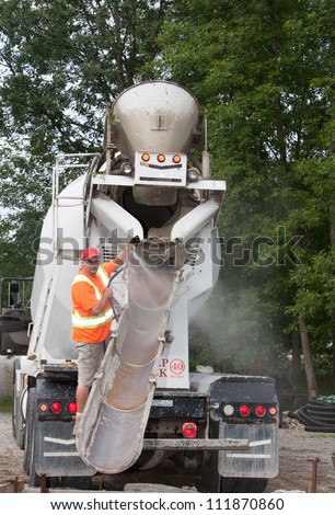 A rear view of a cement truck being readied by its operator to pour cement down the chute.