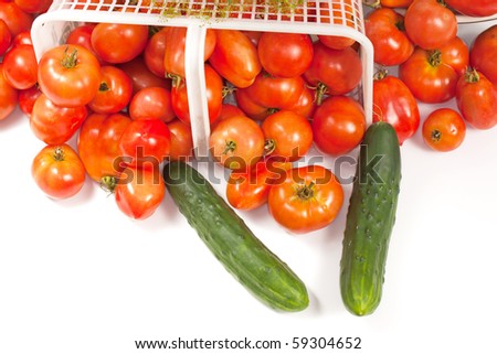An angled studio view of a basket of ripe field tomatoes with a sprig of dill and a couple of cucumbers.
