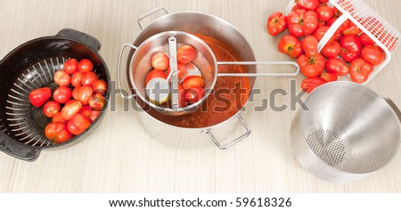 A top studio view a a stainless steel hand mill and fresh Field tomatoes in colanders.