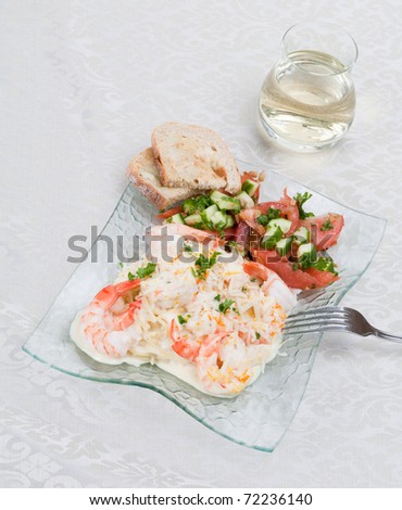 An angled top view garlic shrimp linguine with a mandarin-garlic cream sauce; side of a tomatoes,cucumbers and parlsey salad and garlic toast; glass of white wine on an off-white cotton tablecloth
