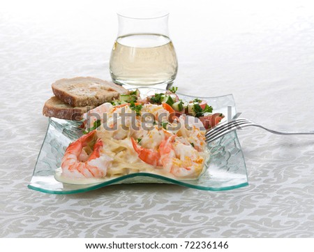 A front portrait view garlic shrimp linguine with a mandarin-garlic cream sauce; side of a tomatoes,cucumbers and parlsey salad; garlic toast; glass of white wine on an off-white cotton tablecloth