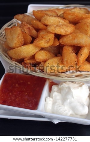 A basket of potato wedges with sour cream and sweet chili sauce