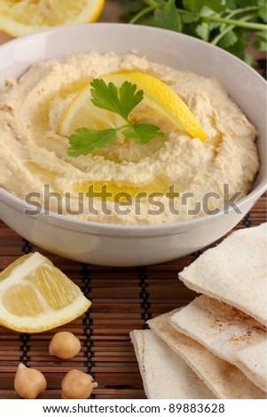 A bowl of homemade hummus served with pitta bread and garnished with olive oil, parsley and lemon.