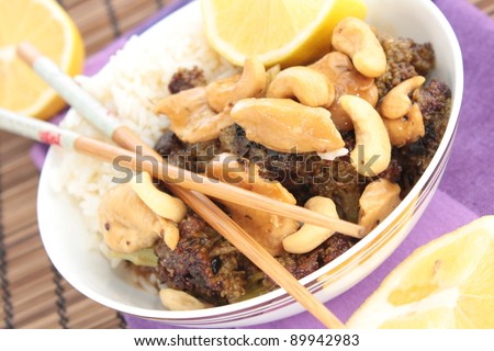 Lemon chicken with broccoli and cashew nuts. Garnished with lemon and served with chopsticks.