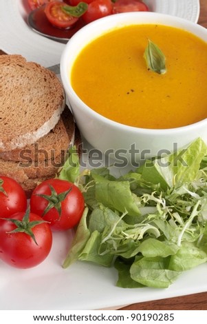 Healthy lunch of carrot soup, cherry tomatoes and lettuce. Served with wholemeal bread on a square plate and with a cherry tomato salad.