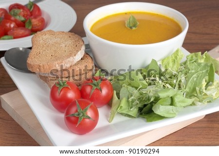 Healthy lunch of carrot soup, cherry tomatoes and lettuce. Served with wholemeal bread on a square plate and with a cherry tomato salad.