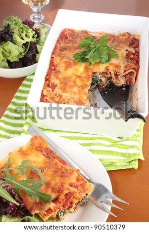 Freshly baked spinach and ricotta cannelloni with a simple green salad. On a green striped cloth and a wooden table. With a glass of wine.