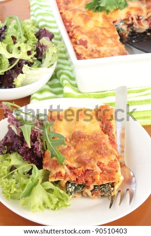 Freshly baked spinach and ricotta cannelloni with a simple green salad. On a green striped cloth and a wooden table.