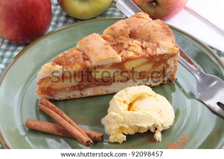 A slice of apple pie with a lattice pastry crust. Decorated with cinnamon sticks and fresh apples.