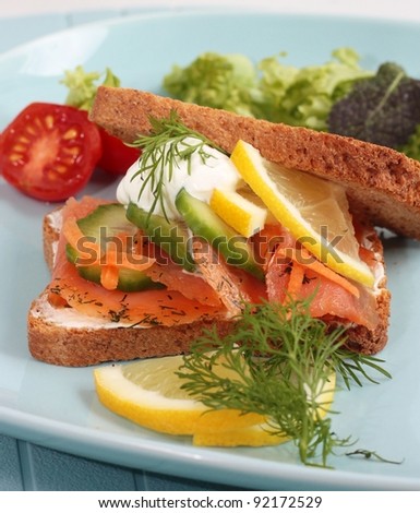 A smoked salmon sandwich on wholemeal bread. With cucumber, sour cream, lemon and dill. Garnished with salad.