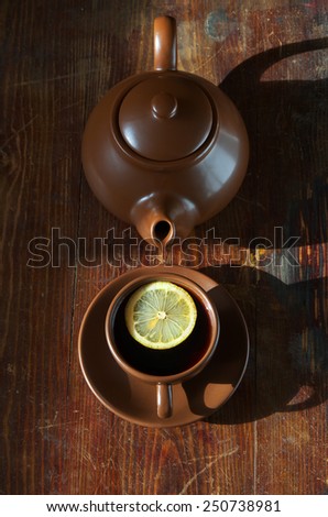 Tea with lemon. Tableware from dark ceramics. Cup of tea and teapot on old wooden table. top view
