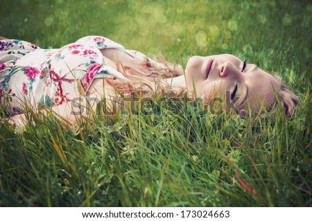 Portrait Of A Young Blonde Woman Lying On Grass With Eyes Shut.