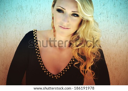 Young beautiful blonde woman with curly hair, smoky eye make-up wearing a black long sleeved dress with golden studs.