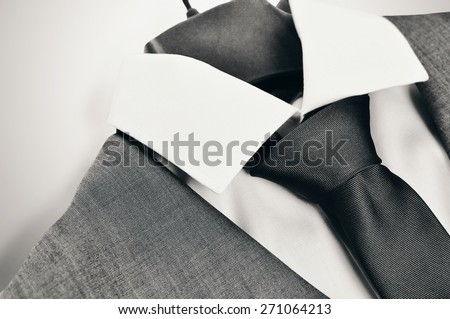 Black and white close-up of an elegant mans suit, collar and tie on clothes hanger on light grey background.