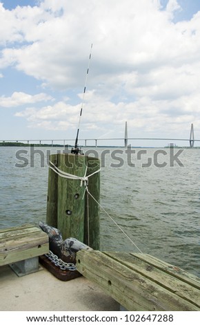 A fishing pole on a pier with the Arthur Ravenel Jr. Bridge over the port of Charleston.