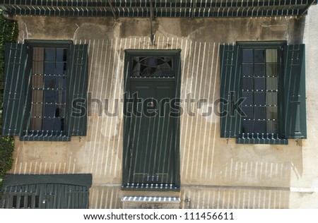 The iron bars of a balcony cast a grilled patterned shadow over the front door of an eighteenth century house in the French Quarter of Charleston, South Carolina.